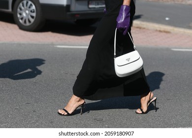 Milan, Italy - September 24, 2021:  Street Style Outfit, Fashionable Woman Wearing A Long Prada Black Dress, Purple Gloves, Prada Earings And White Prada Bag On The Streets Of Milan, Italy.