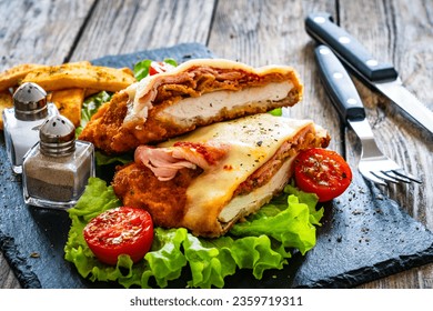 Milanesa Napolitana - fried breaded cutlet with ham, mozzarella cheese and tomato sauce on wooden background 