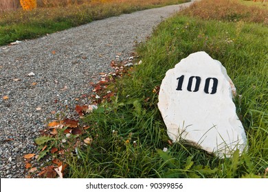 Mile Stone In The Grass Near The Road, With Print Number Hundred Sign