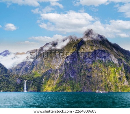 Milford Sound mountain peaks and scenic waterfalls in New Zealand with passenger tourist cruise boat at Stirling fall.