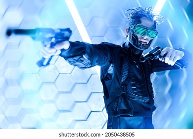 Militant Cyberpunk Warrior In A Protective Suit Shooting His Guns In A Fight In Neon Light Background. World Of The Future. Game, Virtual Reality.