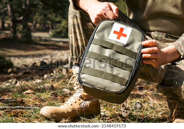 Military army first aid kit. Camouflaged\
soldier medic. White and red first aid\
sign.