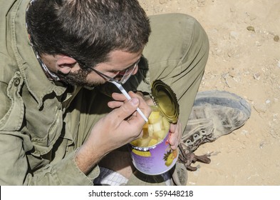 MILITARY BASE, ISRAEL - JUNE 17, 2015: Israeli Army Soldier Holding An Open Tin Can Of Pineapple Slices. Soldier Eating Battle Rations While On A Break During Military Training In The Desert. 