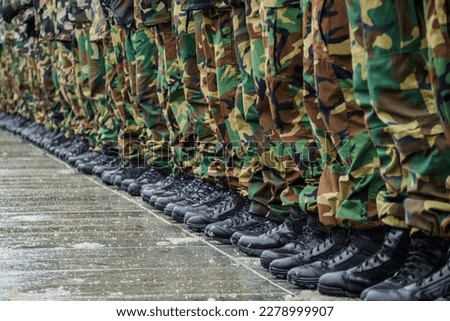 Military boots and camouflage trousers of many soldiers in uniform in a row under the rain and snow