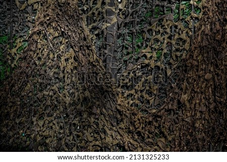 Military camouflage mesh texture background. Dark, brown and green material surface backdrop. Army style camo netting for camping, fishing and hunting. Hiding, staying safe in the forest. Copy space