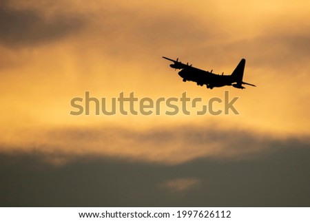 Military cargo jet departing against sunset clouds