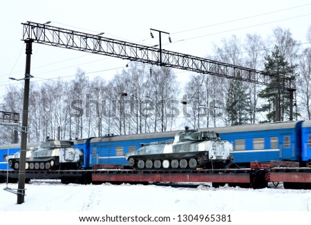 Military combat Soviet tank, artillery tracked vehicle on a railway cargo platform amid a passing blue passenger train at high speed