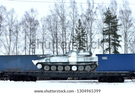 Military combat Soviet tank, artillery tracked vehicle on a railway cargo platform against the background of a cargo sea container passing on rails at high speed