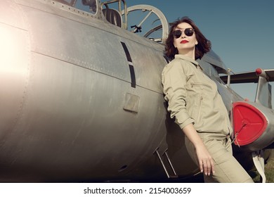 Military and commercial aircraft. Portrait of a confident pilot woman wearing uniform and sunglasses posing next to her fighter jet. 