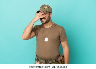Military With Dog Tag Over Isolated On Blue Background Covering Eyes By Hands And Smiling