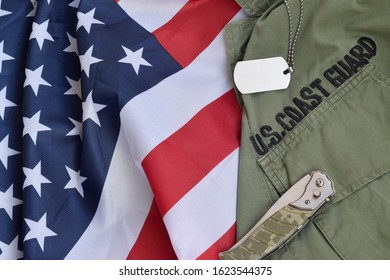Military dog tag token and knife lies on Old US Coast Guard uniform and folded United States Flag