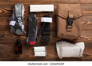 Military first aid kit. Medical tourniquet to stop the blood, alcohol, bandages and cotton wool on a brown textured wood. Place to copy. View from above. Flat lay.