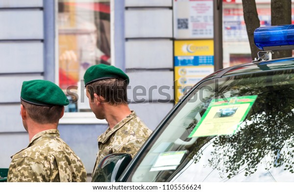 Military in green berets stand near the car.\
Soldiers in a camouflage on the city\
street