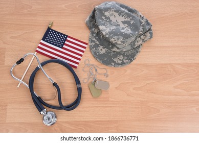 Military Health Care Concept. Light Wood Background With Stethoscope, American Flag, Camo Hat, And Dog Tags.