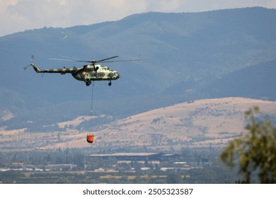 A military helicopter carries water with a helicopter bucket (helibucket). - Powered by Shutterstock