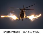 Military helicopter in flight firing off flare decoys at night.