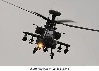 A Military helicopter in flight with a front light on during a cloudy day