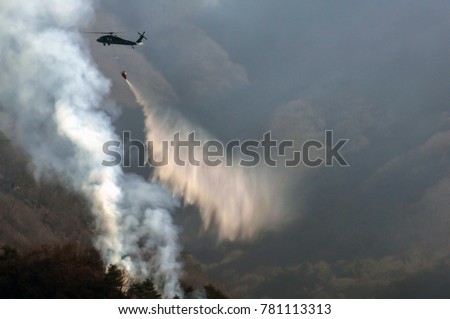 A Military helicopter sprinkle water to put out a forest fire.