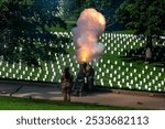 A military honor guard firing a cannon salute in a cemetery with rows of white headstones