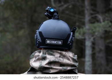 Military instructor in a tactical helmet with a night vision monocular in the forest at dusk. View from the back. - Powered by Shutterstock