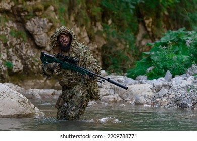 A Military Man Or Airsoft Player In A Camouflage Suit Sneaking The River And Aims From A Sniper Rifle To The Side Or To Target.