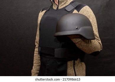 A military man in a bulletproof vest holds an army helmet in his hand, black background. Concept: volunteer at war, war in Ukraine, civil self-defense, army unit.