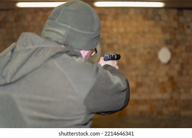 A Military Man In A Green Uniform Shoots A Pistol With A Silencer In A Shooting Range.