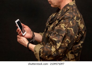 A Military Man In Handcuffs Makes A Phone Call On A Dark Background, Selective Focus. Concept: Prisoner Of War Talking On The Phone, Prisoner Exchange.