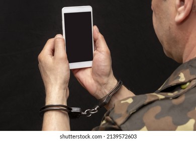 A Military Man In Handcuffs Makes A Phone Call On A Dark Background, Selective Focus. Concept: Prisoner Of War Talking On The Phone, Prisoner Exchange.