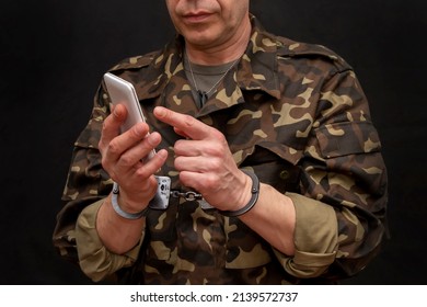 A Military Man In Handcuffs Makes A Phone Call On A Dark Background, Selective Focus. Concept: Prisoner Of War Talking On The Phone, Prisoner Exchange.