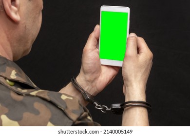 A Military Man In Handcuffs Makes A Phone Call On A Dark Background, Selective Focus. Concept: Prisoner Of War Talking On The Phone, Prisoner Exchange.