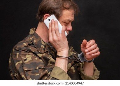 A Military Man In Handcuffs Makes A Phone Call On A Dark Background, Selective Focus. Concept: Prisoner Of War Talking On The Phone, Prisoner Exchange.