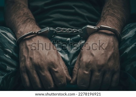 A military man in handcuffs on a dark background, selective focus. Concept: war criminal, prisoner of war, tribunal for deserters, traitor to the Motherland. a prisoner of war under interrogation.