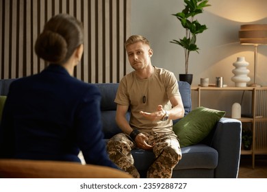 Military man hugging himself suffering from bad memories during therapy session - Shutterstock ID 2359288727