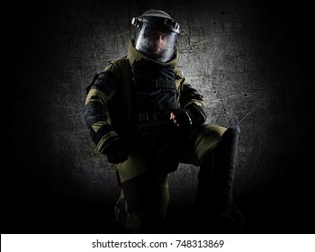 Military man in a protective sapper suit is kneeling and is preparing to neutralize the bomb. Mixed media