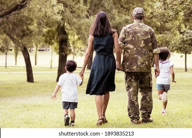 Military Man Walking In Park With His Wife And Children, Kids And Parents Holding Hands. Full Length, Back View. Family Reunion Or Military Father Concept