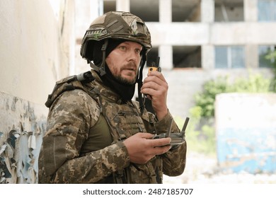 Military mission. Soldier in uniform with drone controller and radio transmitter near abandoned building outdoors - Powered by Shutterstock