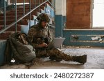 Military mission. Soldier in uniform using laptop inside abandoned building