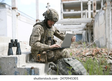 Military mission. Soldier in uniform using laptop near abandoned building outside - Powered by Shutterstock