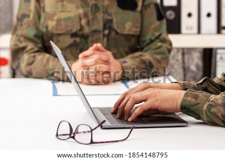 Military officers meet to discuss recruitment. They are using a laptop.