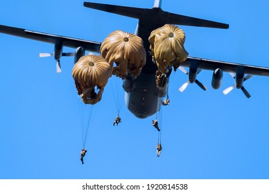 Militärische Fallschirmjäger springen an einem klaren blauen Himmelstag aus einem Flugzeug der Luftwaffe.