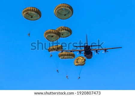 Military parachutist paratroopers parachute jumping out of a air force planes on a clear blue sky day.
