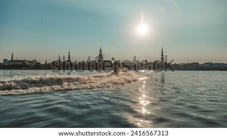 military patrol boat on a mission in a harbor with industrial cranes and cargo ships in the background under a cloudy sky