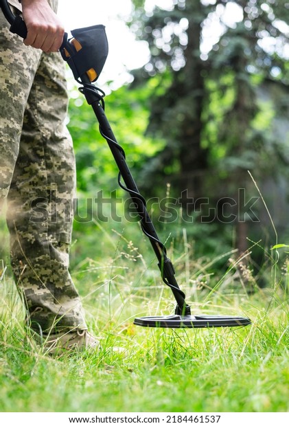 Military sapper with a metal detector in the\
field. Ukrainian Explosive Ordnance Disposal Officer detecting\
metal by metal detector\
device