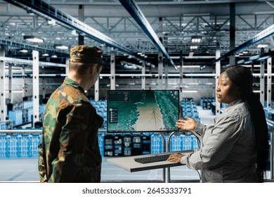 Military server hub personnel discussing target coordinates displayed on digital map interface. Army information expert talking with commander in data center, reviewing live tactical feed on screen