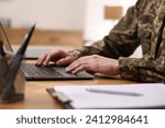 Military service. Soldier working with laptop at wooden table indoors, closeup