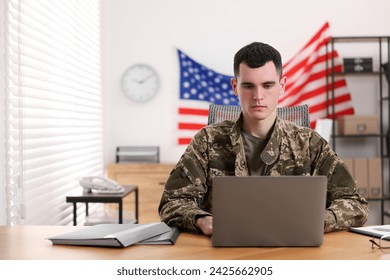 Military service. Young soldier working with laptop at wooden table in office - Powered by Shutterstock