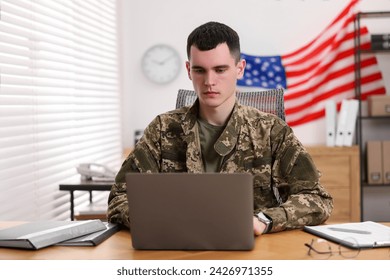 Military service. Young soldier working with laptop at wooden table in office - Powered by Shutterstock