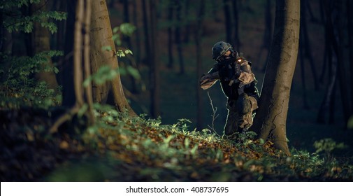 Military Soldier in Action at Night in the Forest Area. Night Time Military Mission. Panoramic Photo. Soldier with Assault Rifle with Flashlight Between Trees.