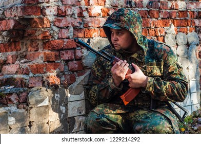 Military Soldier Hid Behind A Brick Wall,waiting Behind Cover.army Tactical Maneuvers. Training At The Military Training Ground.hooded Soldier Close-up. AKS -74. Kalashnikov Assault Rifle